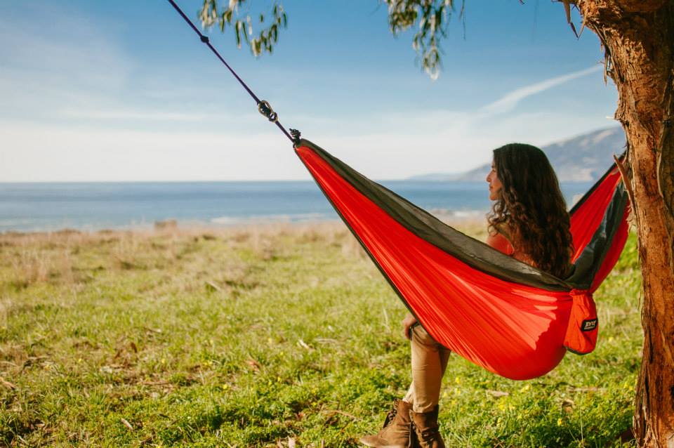 A girl relaxing in an orange Fox Outfitters hammock next to the water
